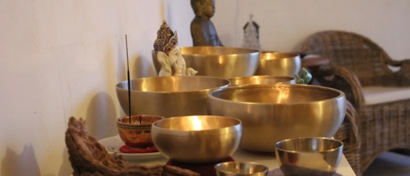 AusKlang am Abend.jpg Mehrere goldene Klangschalen mit Räucherstäbchen in einem stillen Raum mit Meditationsfigur.