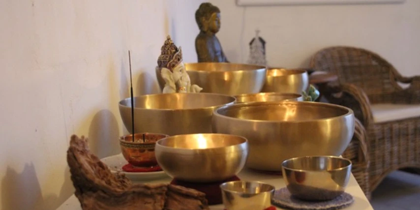 AusKlang am Abend.jpg Mehrere goldene Klangschalen mit Räucherstäbchen in einem stillen Raum mit Meditationsfigur.