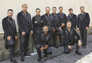 the-ten-tenors-c-the-ten-tenors_rgb.jpg Zehn Männer in dunklen Anzügen posieren selbstbewusst vor einer alten Mauer im Freien.