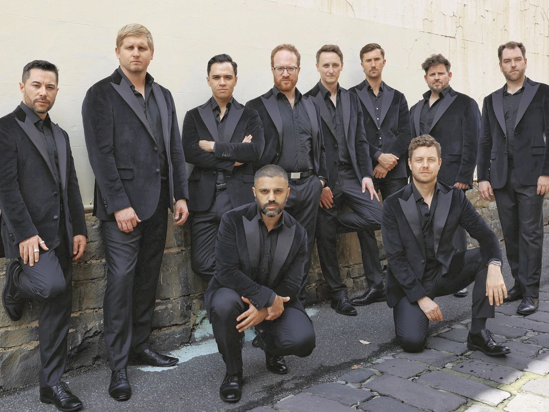 the-ten-tenors-c-the-ten-tenors_rgb.jpg Zehn Männer in dunklen Anzügen posieren selbstbewusst vor einer alten Mauer im Freien.