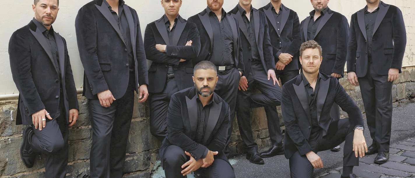 the-ten-tenors-c-the-ten-tenors_rgb.jpg Zehn Männer in dunklen Anzügen posieren selbstbewusst vor einer alten Mauer im Freien.