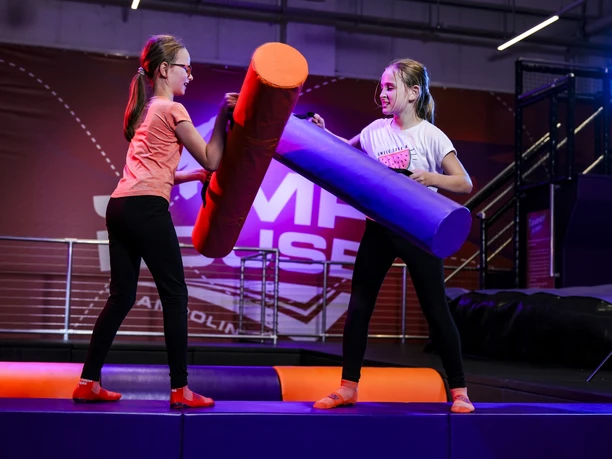 Battle Box im JUMP House Leipzig - Freizeitaktivitäten in Leipzig Zwei Mädchen stehen sich mit Schaumstoffwalzen gegenüber und versuchen sich in der Battle Box von einem Balken zu stoßen, Freizeit, Ausflug, Familie
