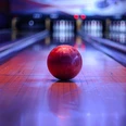 Bowlingbahn Rote Bowlingkugel auf einer beleuchteten Bowlingbahn, im Hintergrund sind verschwommene Kegel zu sehen, die Atmosphäre ist lebhaft und bunt.