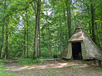 Märchenwald_Köhlerhütte Köhlerhütte zwischen hohen Bäumen im grünen Stadtwald Hube bei Einbeck mit Sitzbänken.