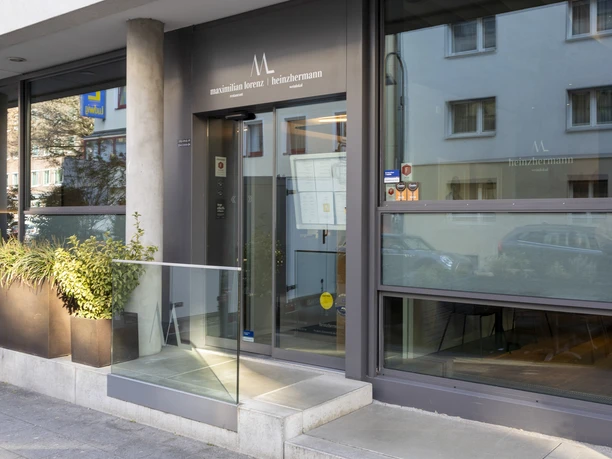 Restaurant Maximilian Lorenz The glass façade of the Maximilian Lorenz restaurant in Cologne reflects the urban lifestyle, while the narrow entrance area invites guests to enjoy an innovative dining experience. Plant decorations add green accents.