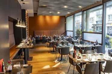 Weinlokal Heinzhermann Ein elegantes Weinlokal mit modernem Interieur, gedeckten Tischen und großen Fenstern, durch die Tageslicht strömt.