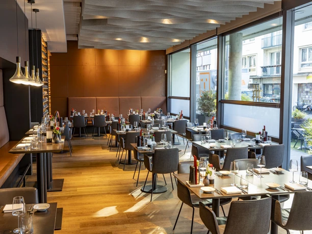Weinlokal Heinzhermann Ein elegantes Weinlokal mit modernem Interieur, gedeckten Tischen und großen Fenstern, durch die Tageslicht strömt.