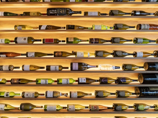 Weinlokal Heinzhermann Weinlokal Heinzhermann zeigt eine stilvolle Wand mit horizontal gelagerten Weinflaschen in beleuchteten Regalen.