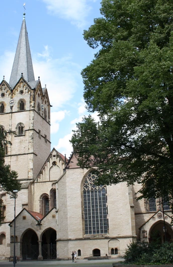 IMG_2607.JPG Historische Kirche mit hohem Turm und gotischen Fenstern umgeben von grünen Bäumen bei sonnigem Wetter.