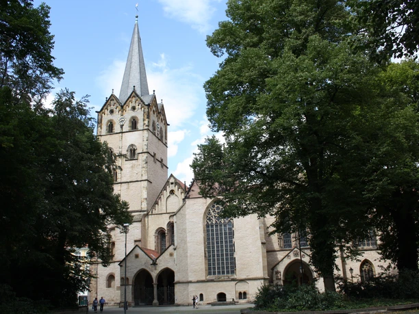IMG_2607.JPG Historische Kirche mit hohem Turm und gotischen Fenstern umgeben von grünen Bäumen bei sonnigem Wetter.