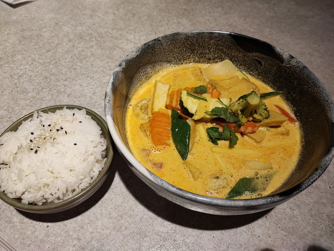 Hähnchen Mango Curry.jpg Eine Schale mit goldgelbem, cremigem Hähnchen-Mango-Curry und bunter Gemüseauswahl. Daneben schneeweißer Reis.