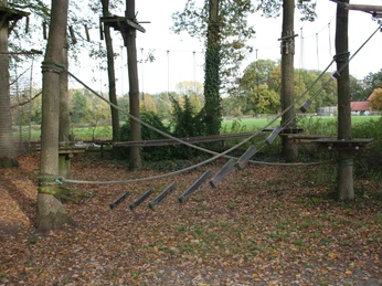 IMG_8236.JPG Kletterpark mit Seilbrücken und Holzleitern im herbstlichen Wald. Blätter bedecken den Boden.