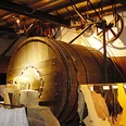Große historische Holztrommel im Inneren eines Gerbereimuseums, beleuchtet von warmem Licht.