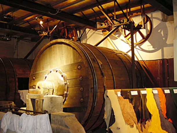 Große historische Holztrommel im Inneren eines Gerbereimuseums, beleuchtet von warmem Licht.