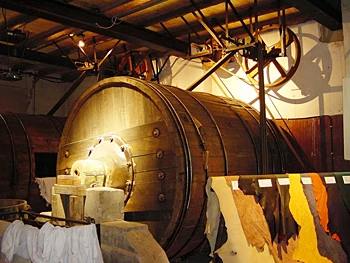 gerbereimuseum-2.jpg Große historische Holztrommel im Inneren eines Gerbereimuseums, beleuchtet von warmem Licht.