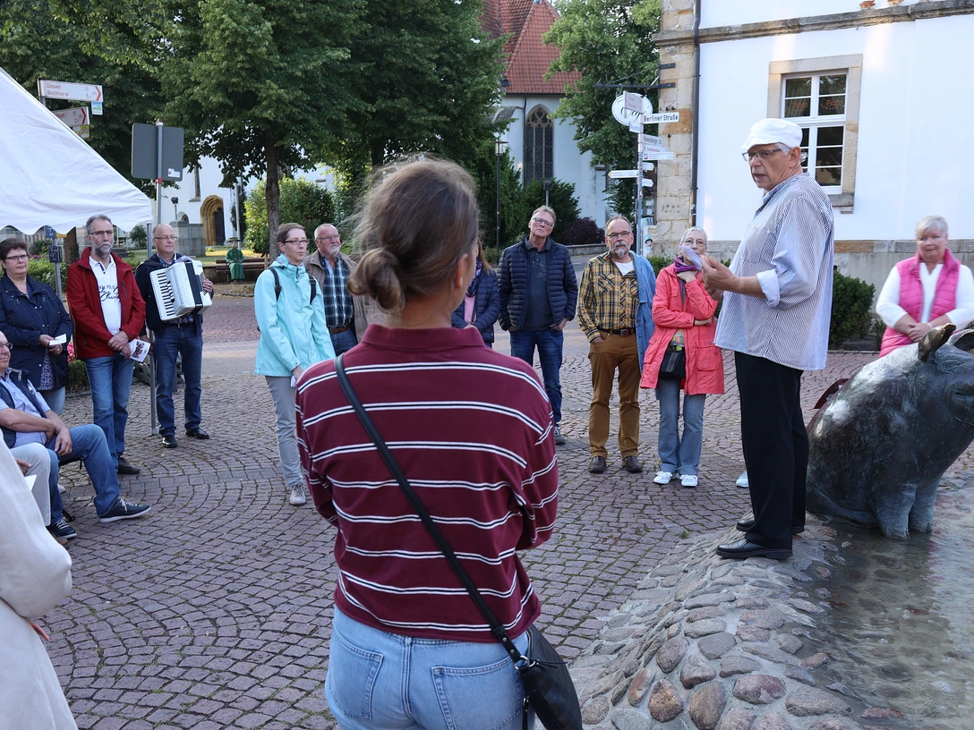 VIP_Fuehrung (4).JPG Eine kleine Menschenmenge hört interessiert einem Mann in historischer Kleidung zu, der auf einem Brunnen steht.