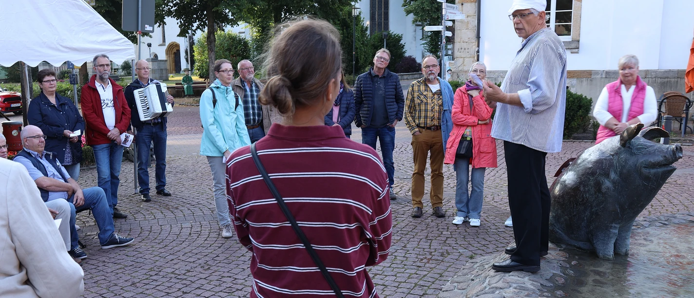 VIP_Fuehrung (4).JPG Eine kleine Menschenmenge hört interessiert einem Mann in historischer Kleidung zu, der auf einem Brunnen steht.