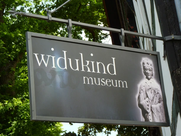 Schild des Widukind Museums mit historischer Abbildung eines mittelalterlichen Königs auf schwarzem Hintergrund.