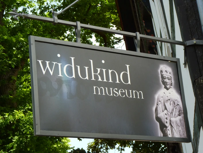 Schild des Widukind Museums mit historischer Abbildung eines mittelalterlichen Königs auf schwarzem Hintergrund.