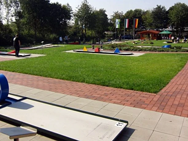 minigolfplatz2.jpg Eine Minigolfanlage mit gepflegtem Rasen, bunten Hindernissen und teils schattigen Plätzen im Freien.