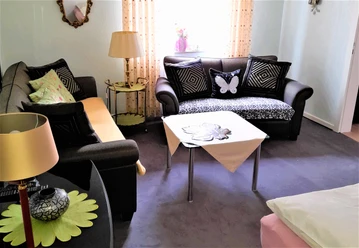 Wohnzimmer mit zwei Sofas, dekorativen Kissen, Beistelltisch, Stehlampe und großen Fenstern.