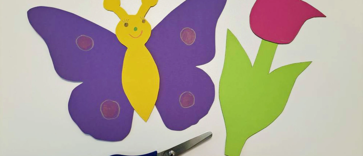 Basteln mit Tonkarton Ein bunter Schmetterling aus Tonkarton, eine Schere und ein Kleber auf einem Tisch.