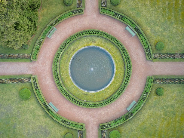 Parkanlage Schloss Weesenstein Kreisförmiger Garten des Schloss Weesenstein mit zentralem Brunnen, umgeben von grünen Hecken und Blumenbeeten, mit vier Bänken auf den Wegen.