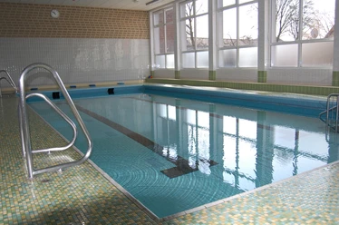 Innenbereich Hallenbad Clarholz.JPG Schwimmhalle mit türkisfarbenem Becken, Stufen- und Railing-Zugang, großen Fenstern und heller Kachelwand.
