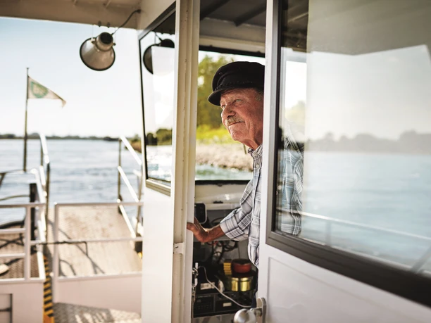 Piwipper Böötchen in Monheim am Rhein Ein älterer Mann in Uniform steht an Bord eines kleinen Flussbootes und blickt auf den Rhein.