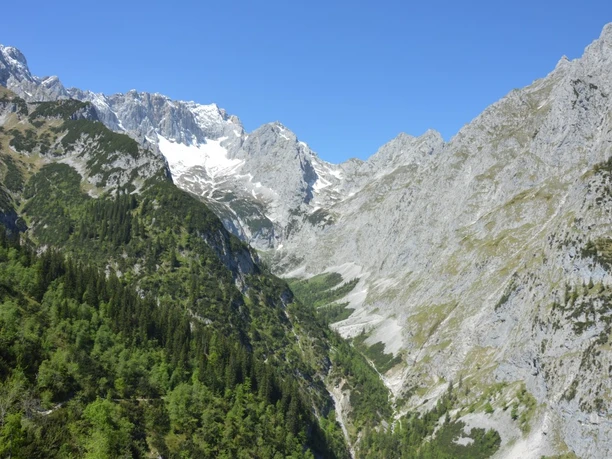 Blick vom Höllental bis hinauf auf die Zugspitze - und mittendrin die Höllentalangerhütte Weitreichendes alpines Tal mit Felswänden, grünen Hängen und schneebedecktem Gipfel.