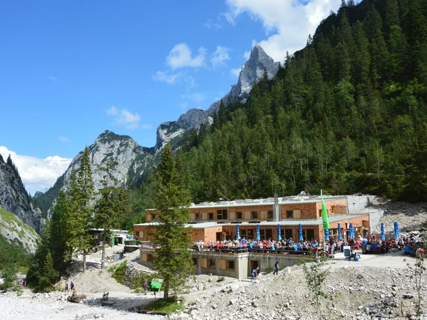 von der Südseite Holzberghütte vor steilen Felswänden mit vielen Rastenden und umliegendem Wald