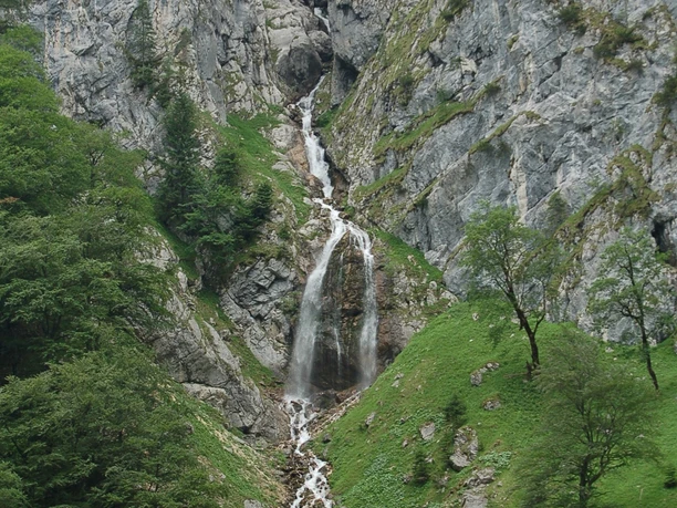 Eine Felswand vor der Höllentalklamm Steiler Wasserfall stürzt durch eine felsige Klamm, umgeben von grün bewachsenen Hängen