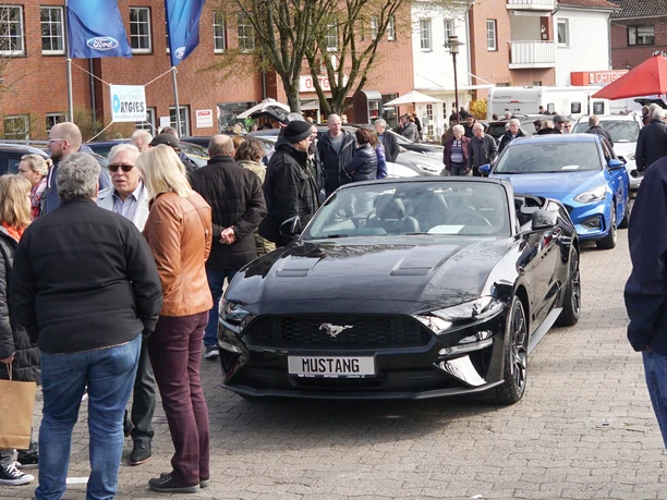Automesse Ein schwarzer Mustang Cabrio steht im Mittelpunkt einer gut besuchten Automesse im Freien.