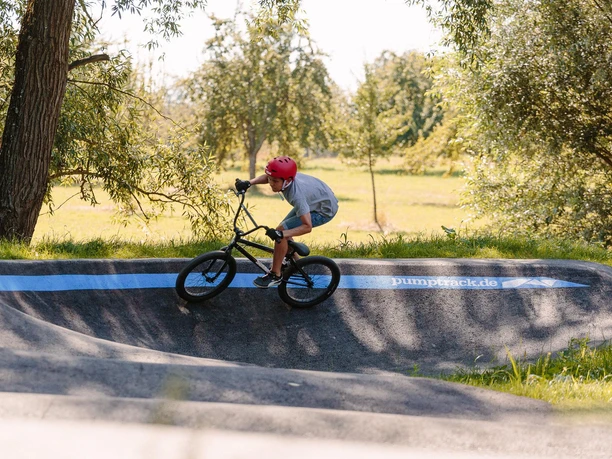 Ein Junge mit rotem Helm fährt auf einem BMX-Rad eine kurvige Asphaltstrecke entlang.