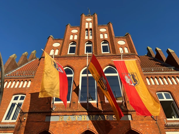 Historisches Backstein-Rathaus Stolzenau mit deutschen Flaggen im Vordergrund unter klarem Himmel.