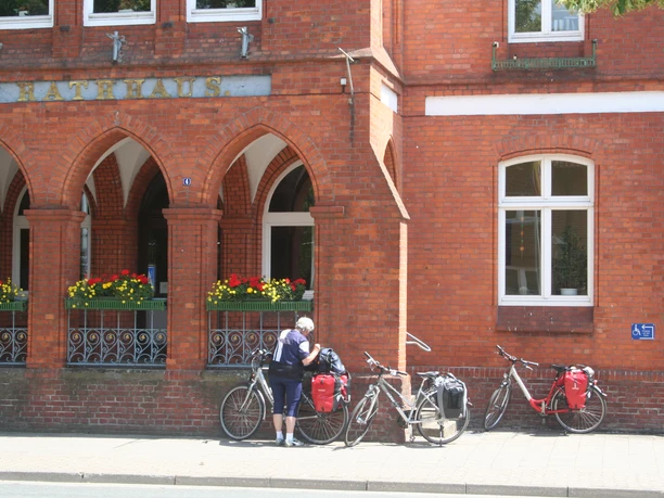 Rathaus Stolzenau Rotes Backsteingebäude mit Arkaden, vier Fahrräder und eine Person in Sportkleidung bei den Rädern.