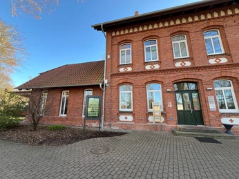 Infoterminal Stolzenau am alten Bahnhof Historisches Backsteingebäude mit Infoterminal, umgeben von einem gepflasterten Vorplatz unter blauem Himmel.