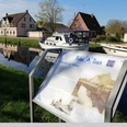 Fehn-Tour.png Infotafel zum historischen Rundgang vor einem Kanal mit Boot und Häusern in Rhauderfehn