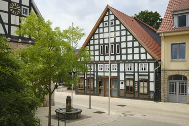 Sachsenhagen (10).jpg Fachwerkgebäude säumen einen kleinen, gepflasterten Platz mit einem dekorativen Brunnen im Vordergrund.