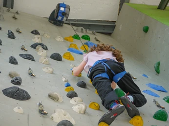 Sicherungsautomat im Kletterbereich Ein Kind klettert eine bunte Kletterwand hoch, gesichert mit einem blauen Klettergurt; die Atmosphäre wirkt konzentriert und sportlich.A child climbs up a colorful climbing wall, secured with a blue climbing harness; the atmosphere is concentrated and sporty.Dítě šplhá po barevné lezecké stěně, zajištěné modrým horolezeckým úvazkem; atmosféra je soustředěná a sportovní.Dziecko wspina się po kolorowej ściance wspinaczkowej, zabezpieczone niebieską uprzężą wspinaczkową; atmosfera jest skoncentrowana i sportowa.Een kind klimt op een kleurrijke klimwand, gezekerd met een blauwe klimgordel; de sfeer is geconcentreerd en sportief.Un bambino si arrampica su una parete da arrampicata colorata, assicurandosi con un'imbracatura blu; l'atmosfera è concentrata e sportiva.
