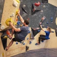 Boulderbereich in der YOYO-Kletterhalle Zwei Personen klettern an einer Indoor-Kletterwand mit bunten Griffen; der Mann trägt ein graues Shirt, die Frau ein blaues.