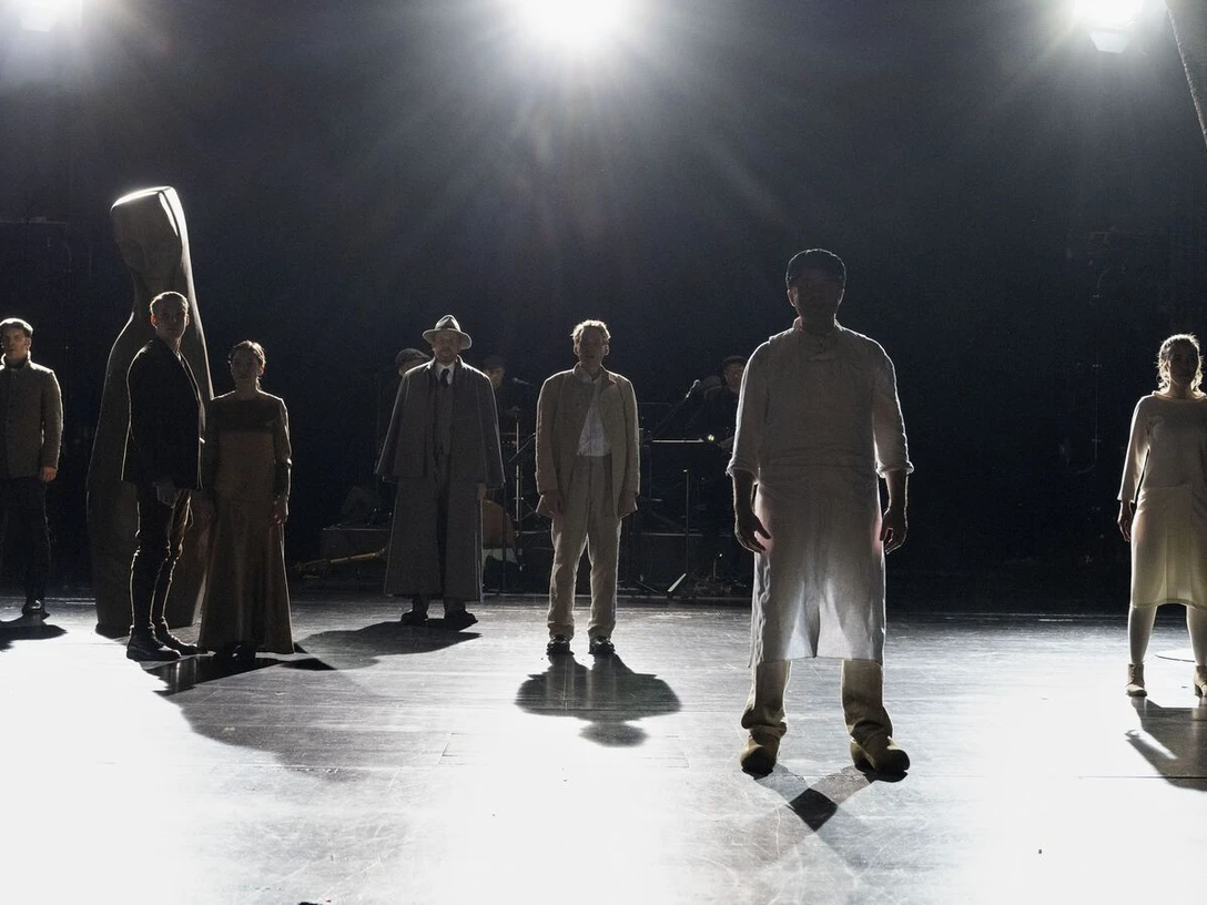 Mehrere Personen stehen im Scheinwerferlicht auf einer Theaterbühne.