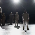 Mehrere Personen stehen im Scheinwerferlicht auf einer Theaterbühne.