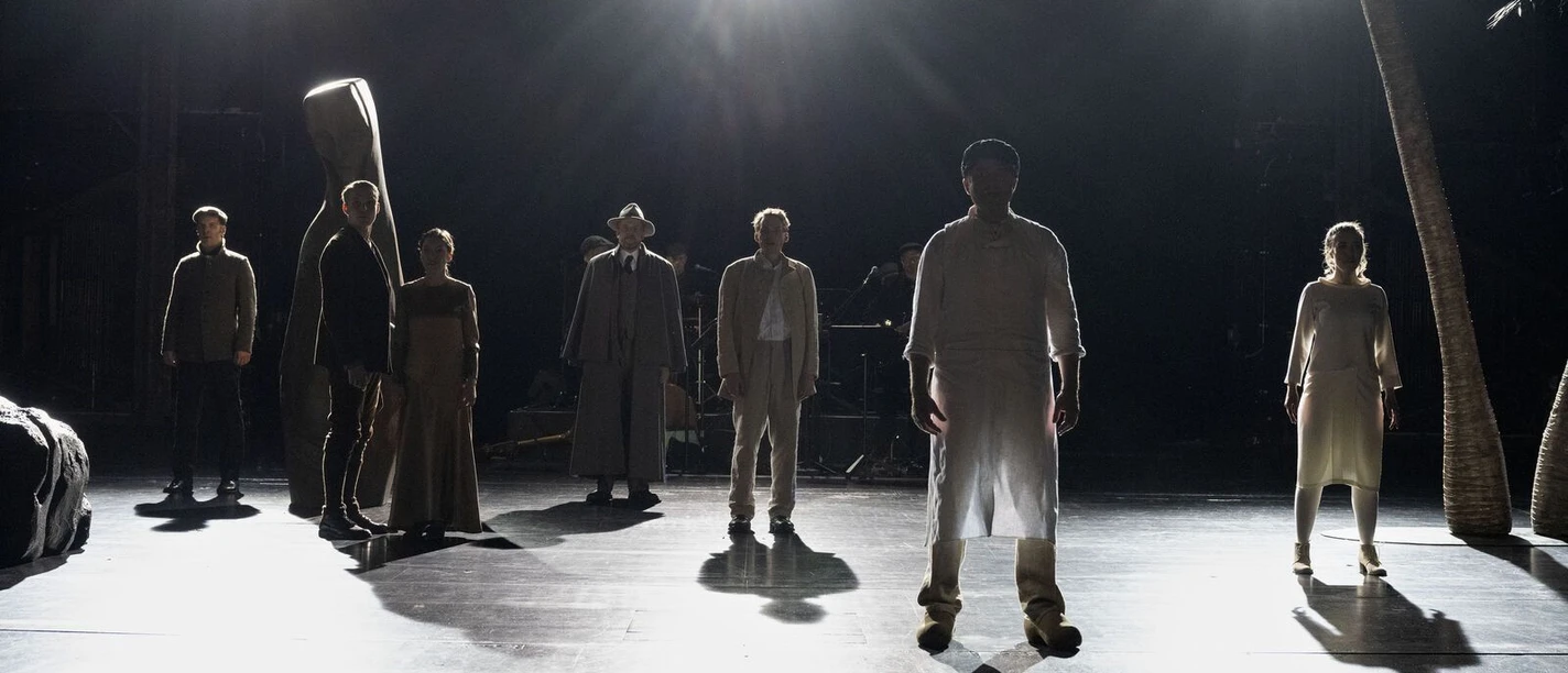 Mehrere Personen stehen im Scheinwerferlicht auf einer Theaterbühne.