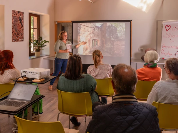 Vortrag im Geoportal Porphyrhaus Zu sehen ist ein Vortrag im Geoportal Porphyrhaus mit zahlreichen Besucherinnen, die alle zum Beamer und der vortragenden Person schauen.