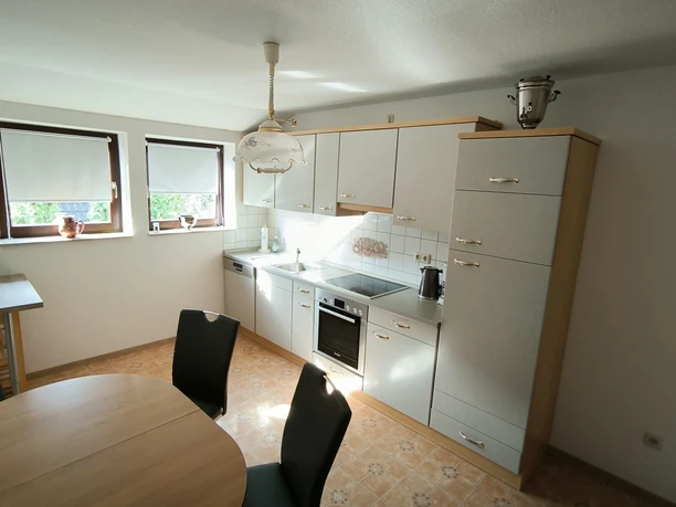 Küche 1.jpg Helle Küche mit Esstisch, Stühlen, moderner Einbauküche, Fenster mit Rollos und Fliesenboden.