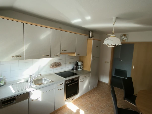 Küche 2.jpg Helle Küche mit moderner Einbauzeile, Esstisch, Stühlen und Zugang zur Terrasse in sonnigem Ambiente.