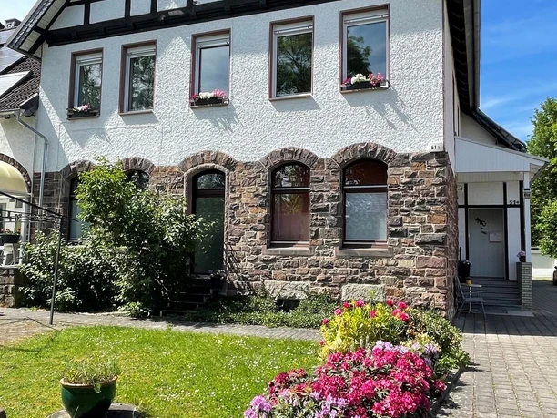 Zweistöckiges Fachwerkhaus mit Steinbasis, blühenden Beeten und gepflegter Rasenfläche im Vordergrund.