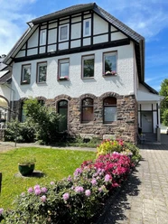 fewo_hermanns_aussenansicht.jpg Zweistöckiges Fachwerkhaus mit Steinbasis, blühenden Beeten und gepflegter Rasenfläche im Vordergrund.