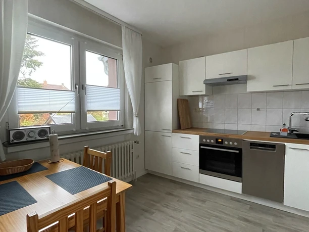 Moderne Küche mit Esstisch für vier Personen, hellen Fronten, großem Fenster und Laminatboden.